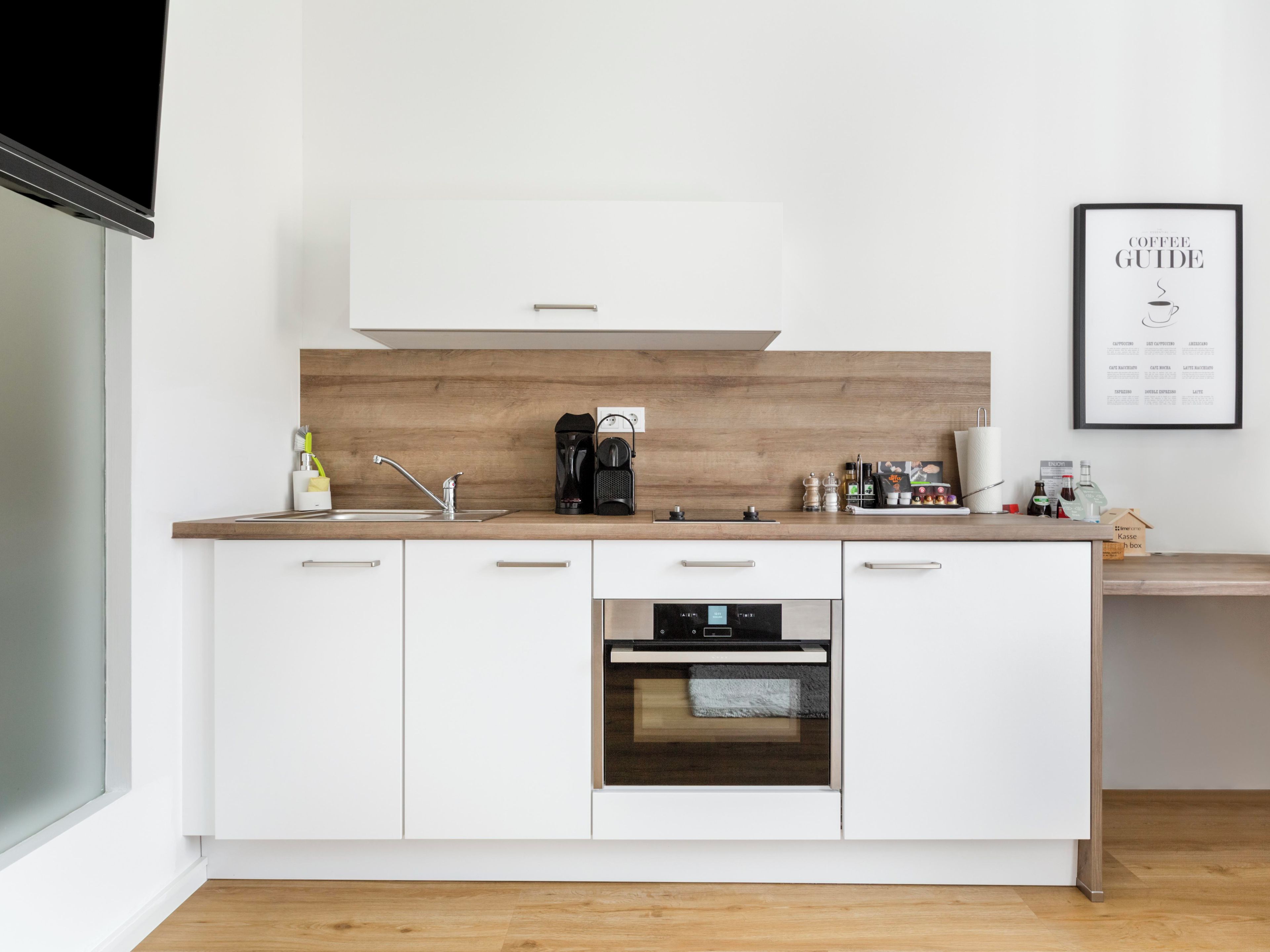 Een moderne keuken met witte kasten, een houten spatwand, een koffiezetapparaat en een koffiehandleiding in een lijst aan de muur.