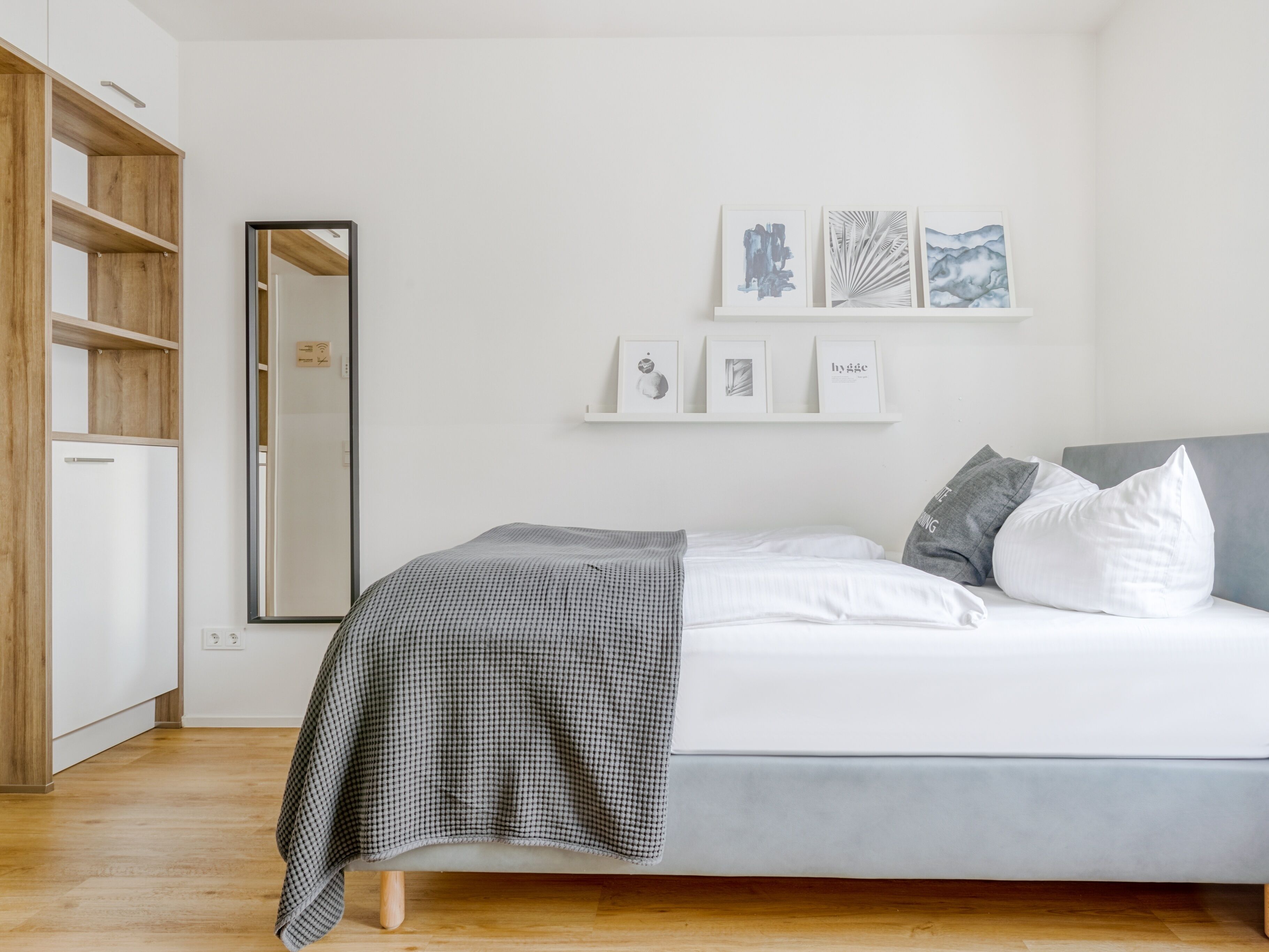 Une chambre à coucher avec un lit, une armoire et un miroir. Trois tableaux encadrés sont accrochés au mur.