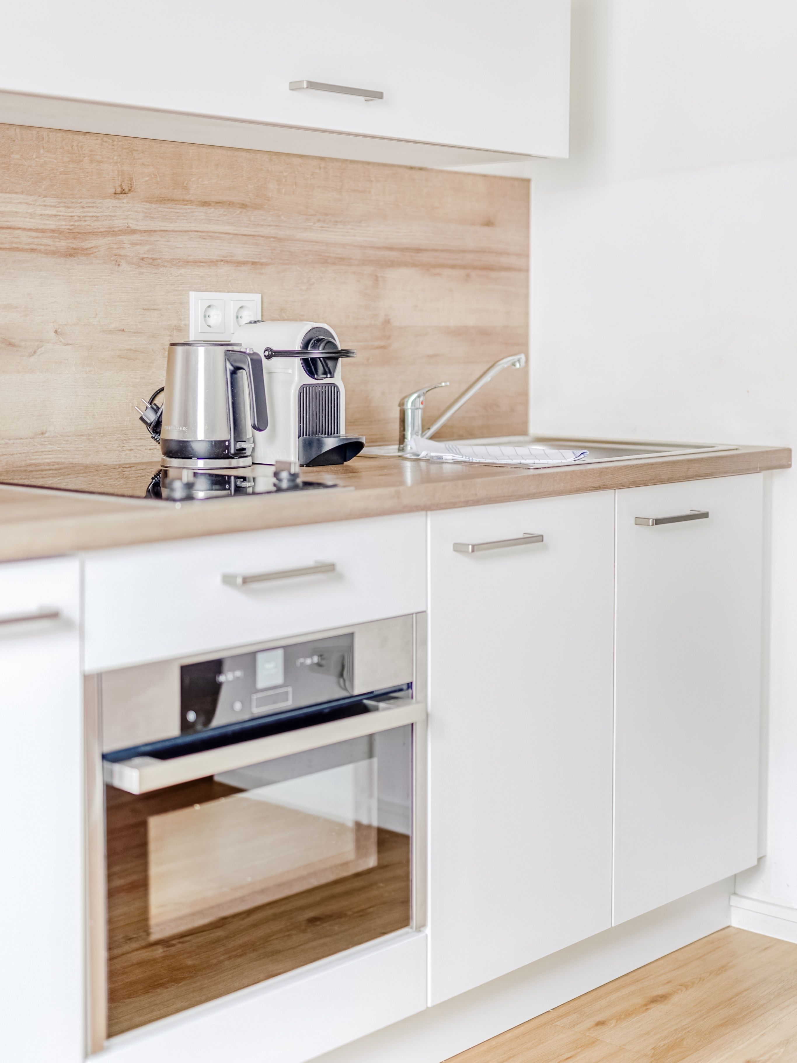 Une cuisine moderne avec des meubles blancs, un plan de travail en bois, une machine à café, un grille-pain et un four.