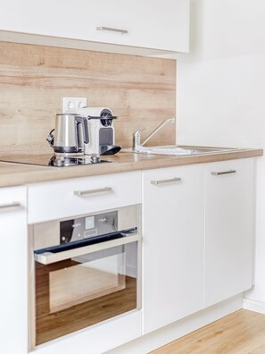 A modern kitchen with white cabinets, a wooden countertop, a coffee maker, a toaster, and an oven. - Limehome Augsburg (Augsburg)