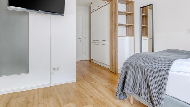 A bedroom with a bed, a TV mounted on the wall, a wardrobe, and a mirror. - Limehome Augsburg (Augsburg)