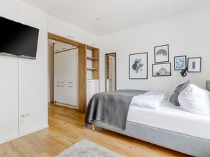 Une chambre à coucher moderne avec un lit, un téléviseur fixé au mur et un dressing.