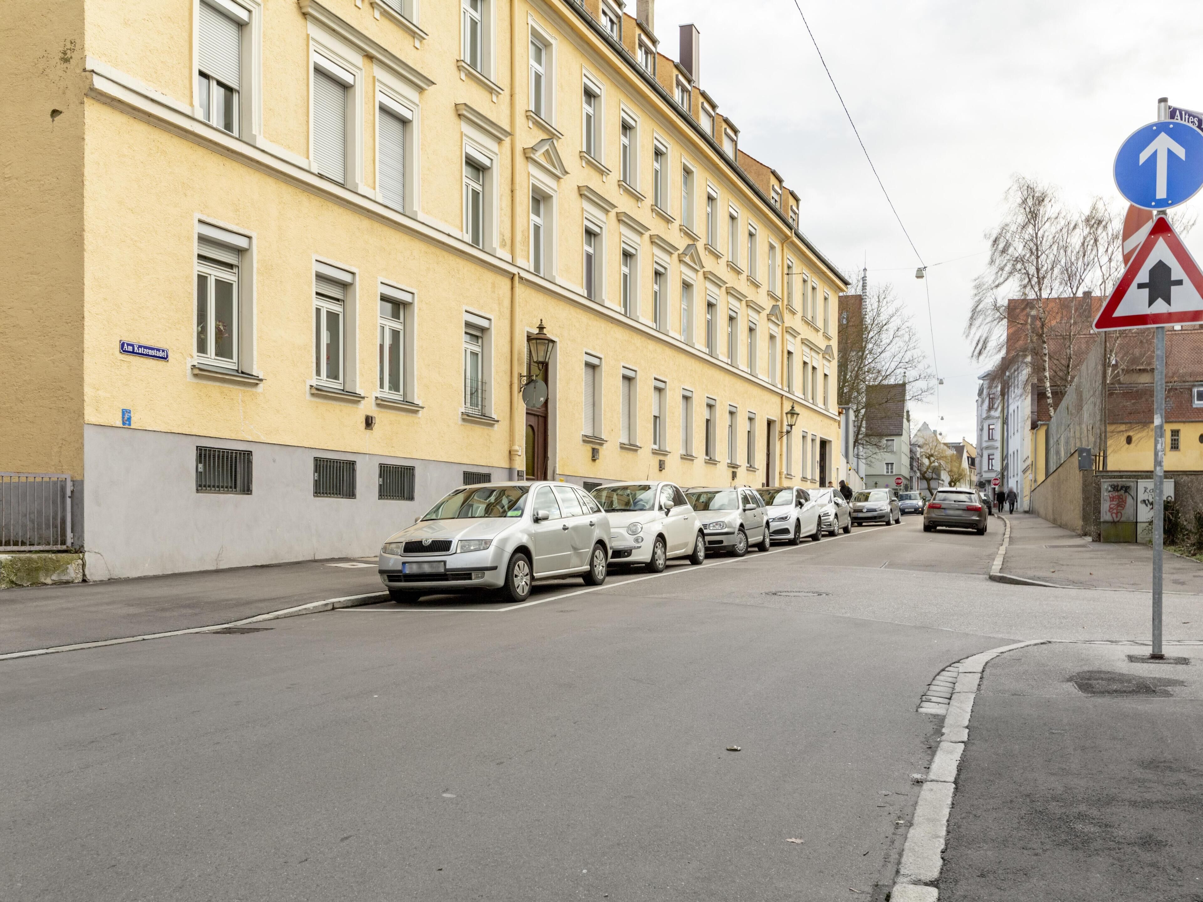 Una strada con auto parcheggiate e un edificio con un cartello che riporta “Am Katresstadel”.