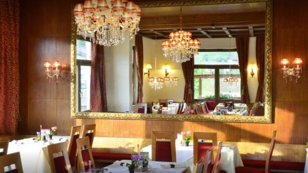 Comedor con un espejo grande, candelabros y paneles de madera. Las mesas están dispuestas con manteles blancos y sillas rojas.
