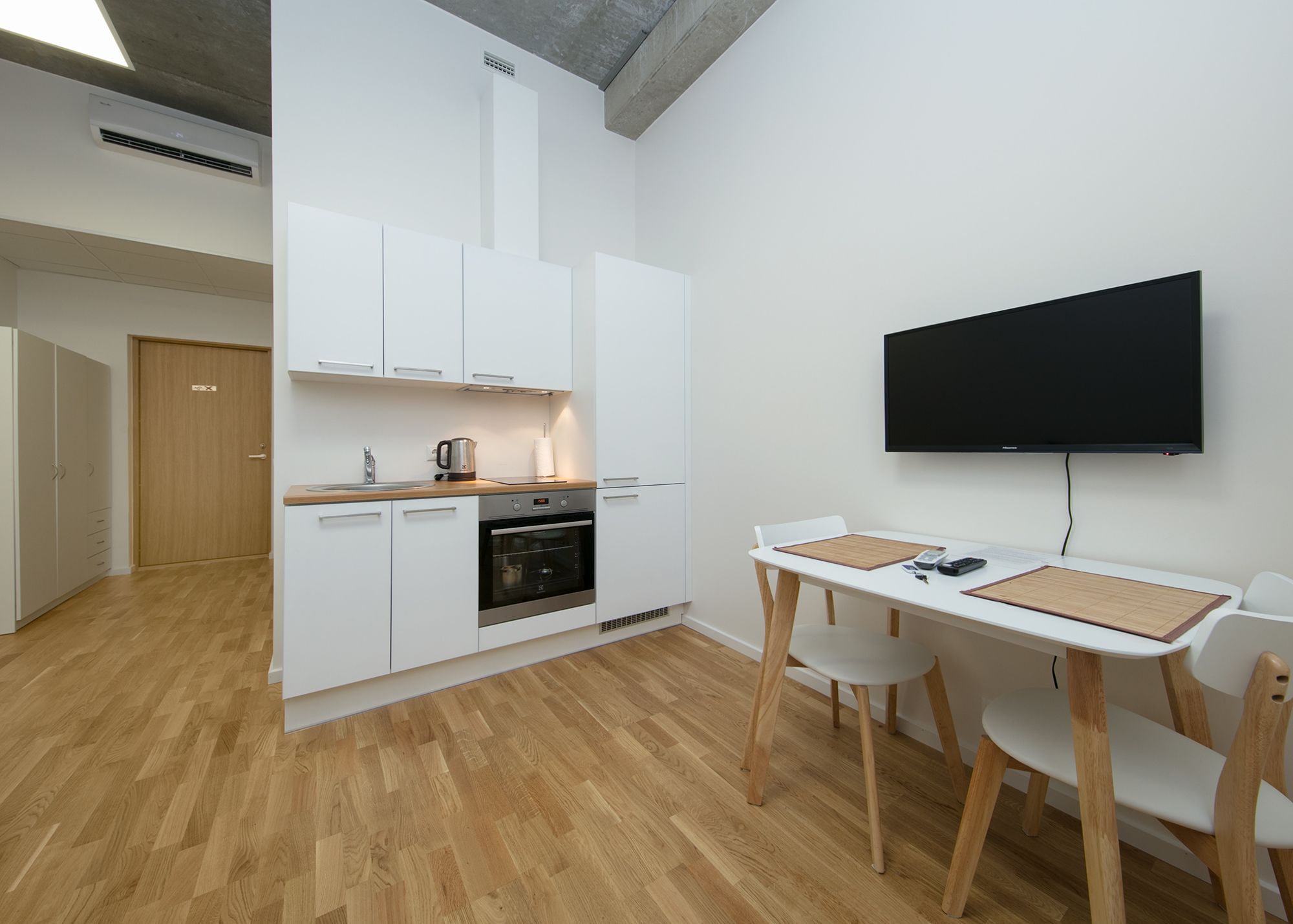 A modern kitchen with white cabinets, a built-in oven, and a dining area with a table and chairs.