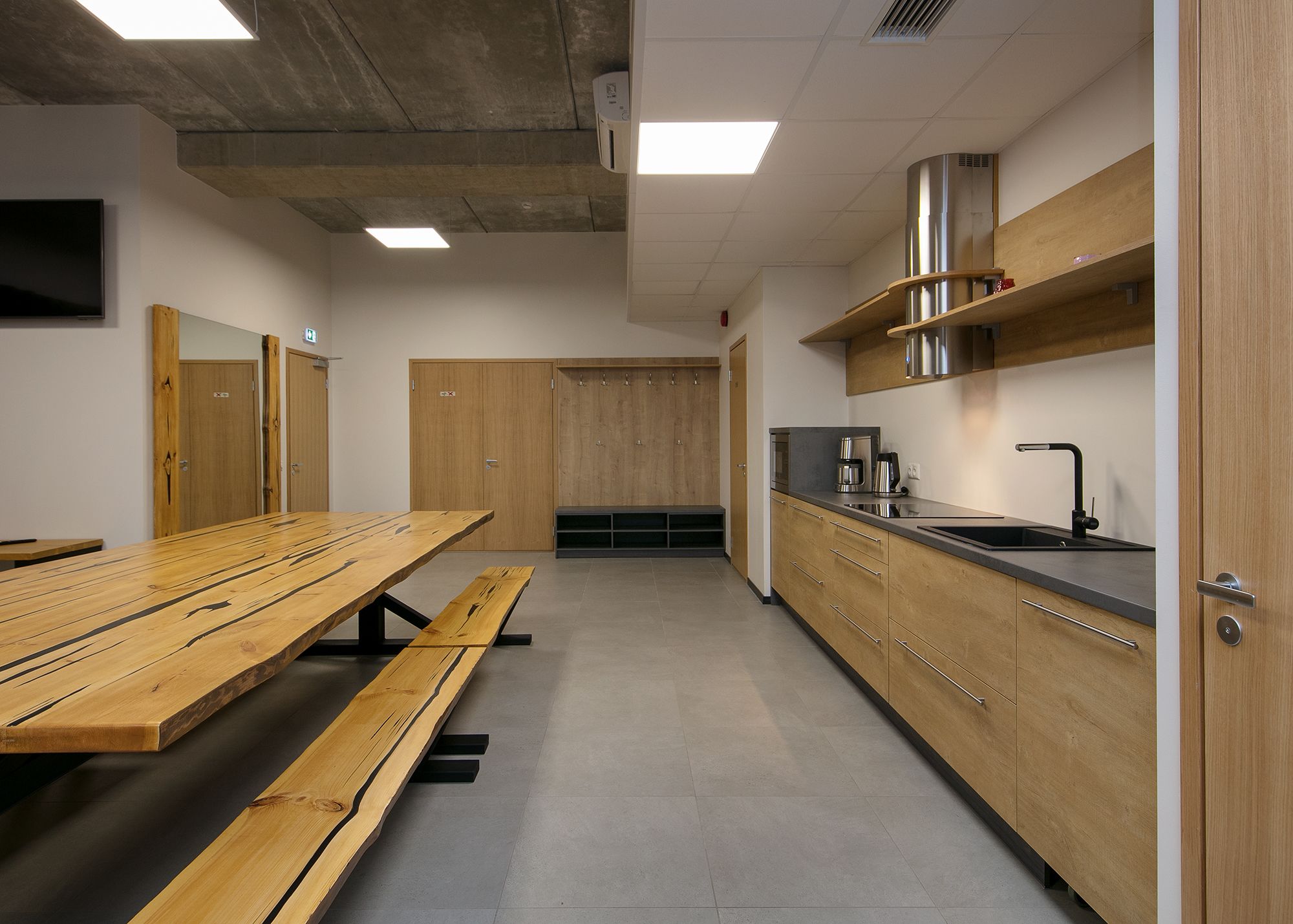 Eine moderne Küche mit Holzausstattung, einem Edelstahlspülbecken und einem langen Holztisch mit Bänken.