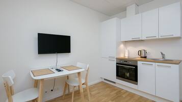 A modern kitchen with white cabinets, a wooden countertop, a built-in oven, and a wall-mounted TV.