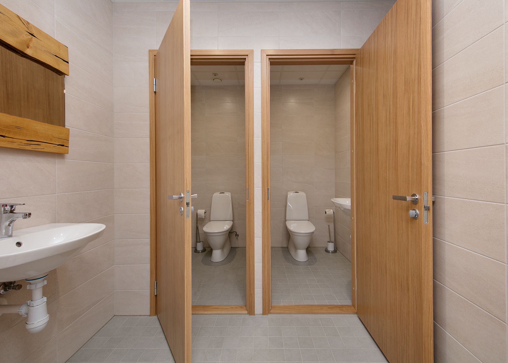 Un bany amb dues vàteres, un lavabo i portes de fusta.