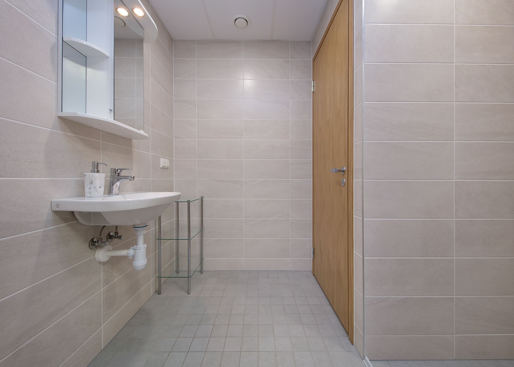 A modern bathroom with a white sink, mirror, and tiled walls.