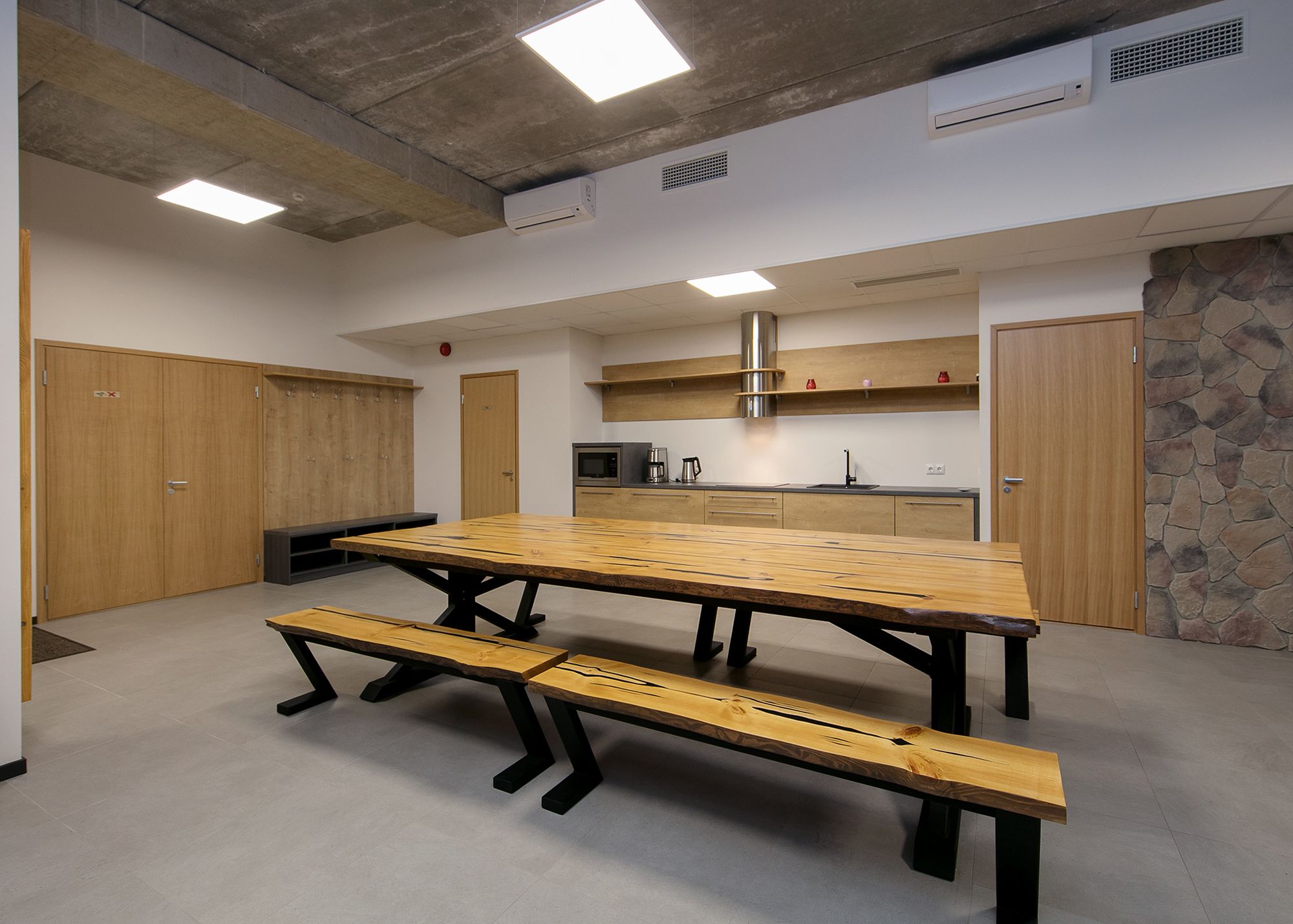 A modern kitchen with a large wooden table and benches, built-in appliances, and a stone accent wall.