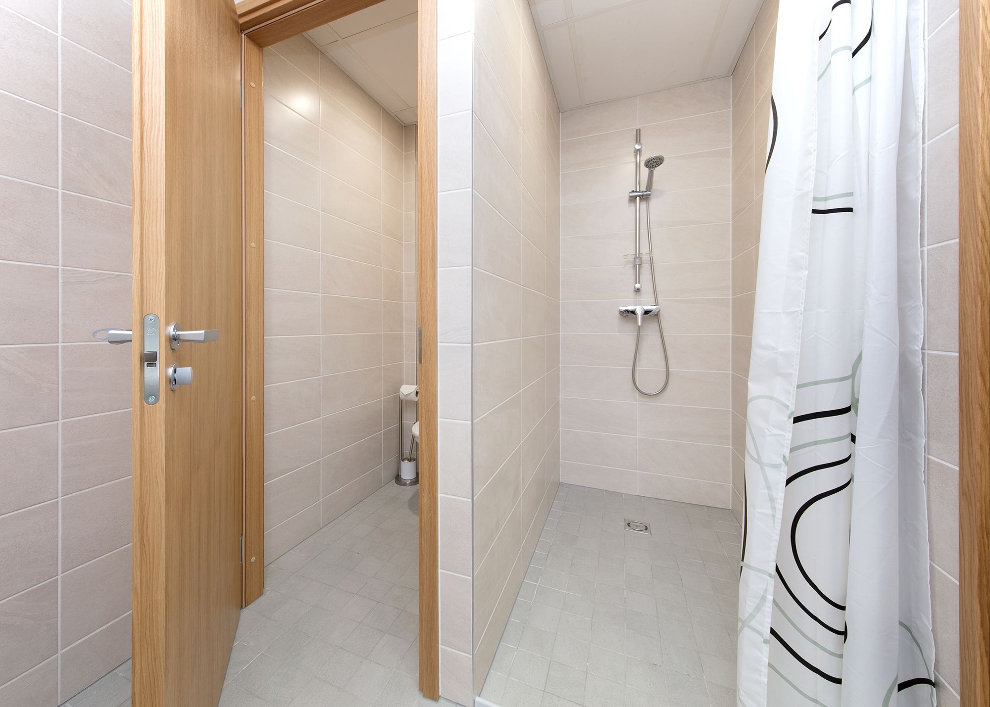 Een kleine, moderne badkamer met een douche, toilet en een houten deur.