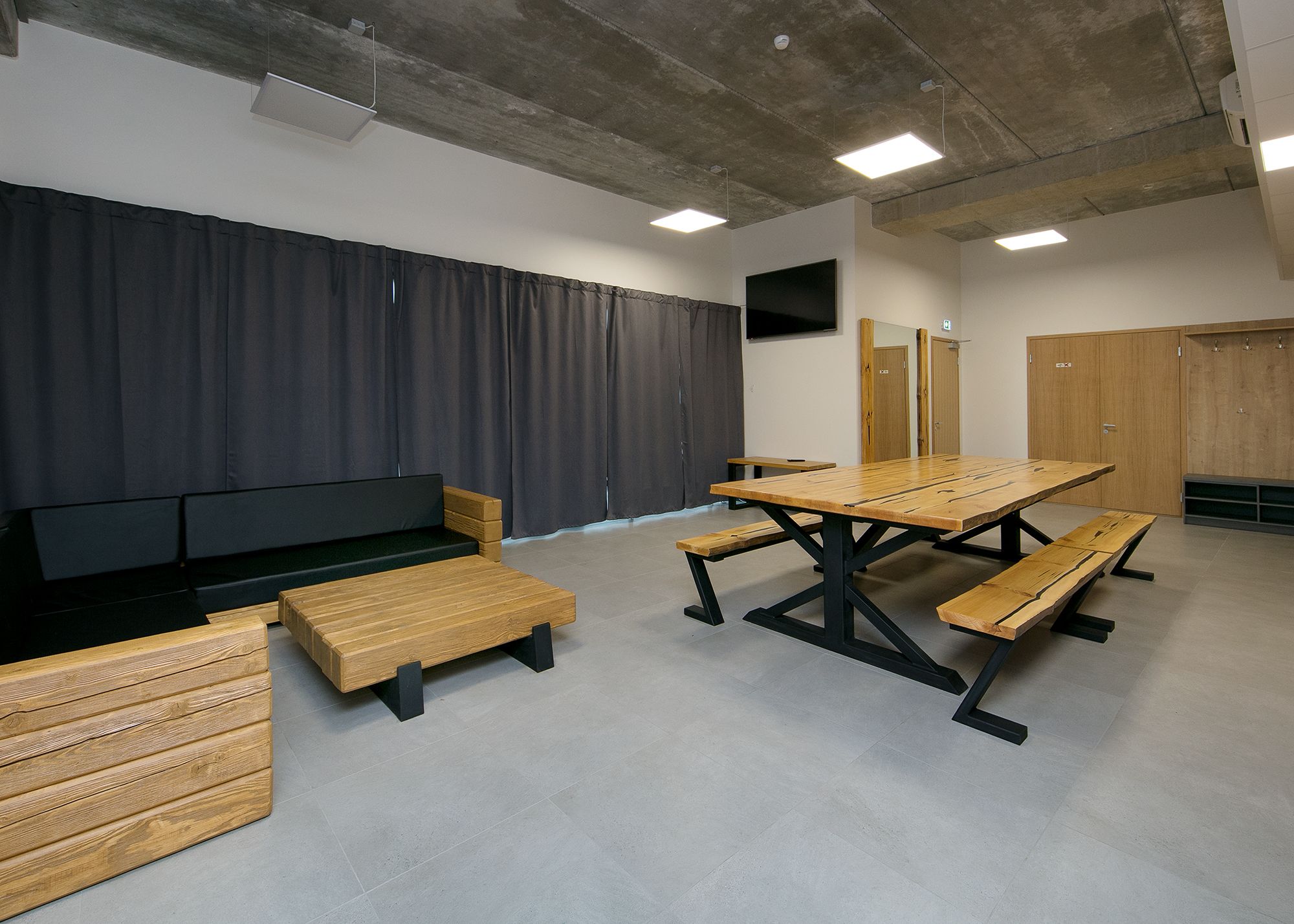 A conference room with a long table, benches, a sofa, and a TV screen.