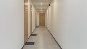 Un pasillo con puertas de madera, piso de baldosas y un detector de incendios en el techo.