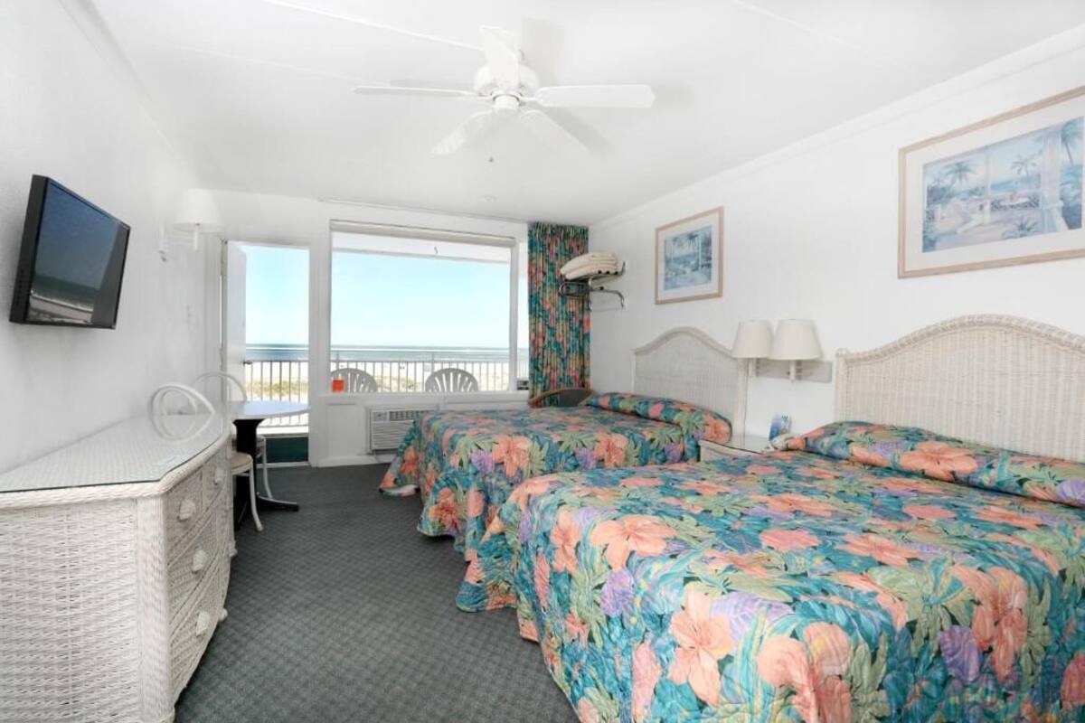 A hotel room with two beds, a television, a desk, and a balcony with a view.