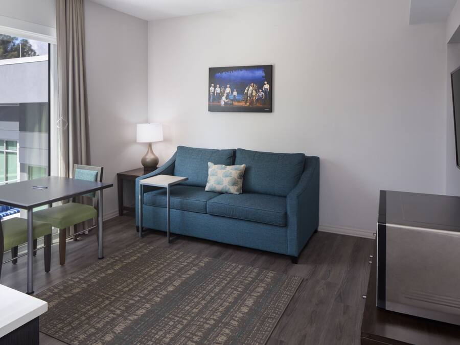 A modern living room with a teal sofa, a small table, a lamp, and a flat-screen TV mounted on the wall.