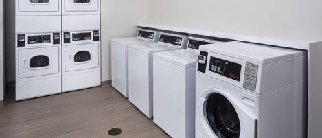 A laundry room with multiple white washing machines and dryers, a wooden floor, and a white wall.