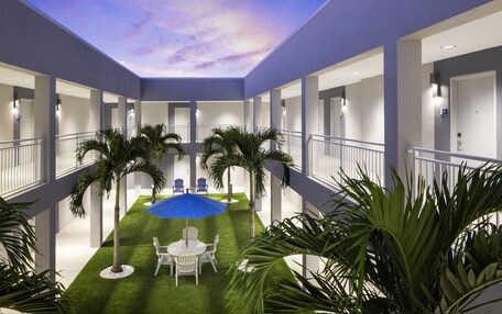 A hotel atrium with a central lawn, palm trees, and a blue umbrella.