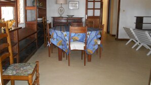 Un comedor con una mesa dispuesta para cuatro personas, rodeada de sillas de madera. Se observa un aparador de madera con objetos decorativos y una lámpara sobre la mesa.