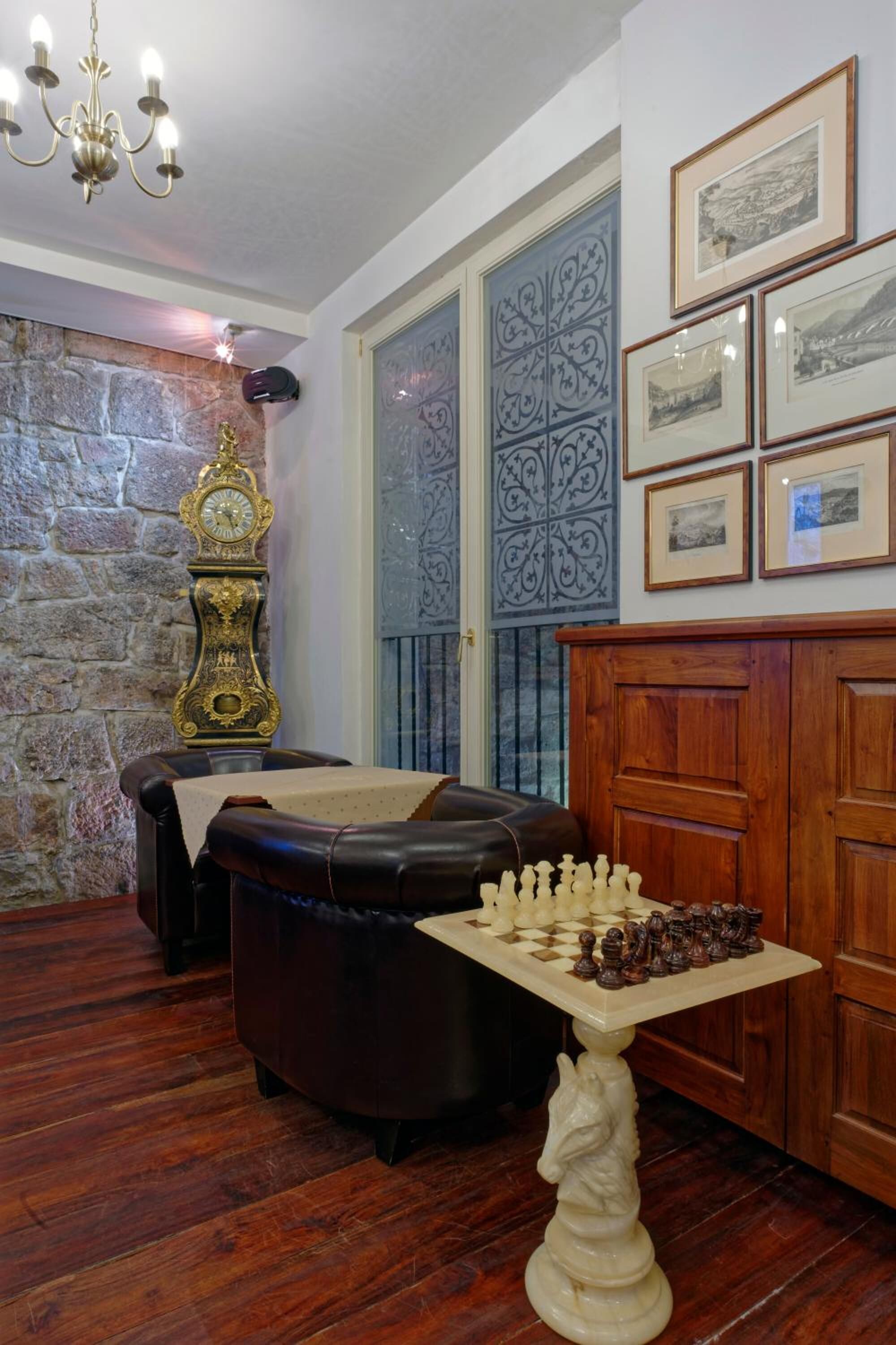 A room with a chessboard on a pedestal, a clock, and framed pictures on the wall.