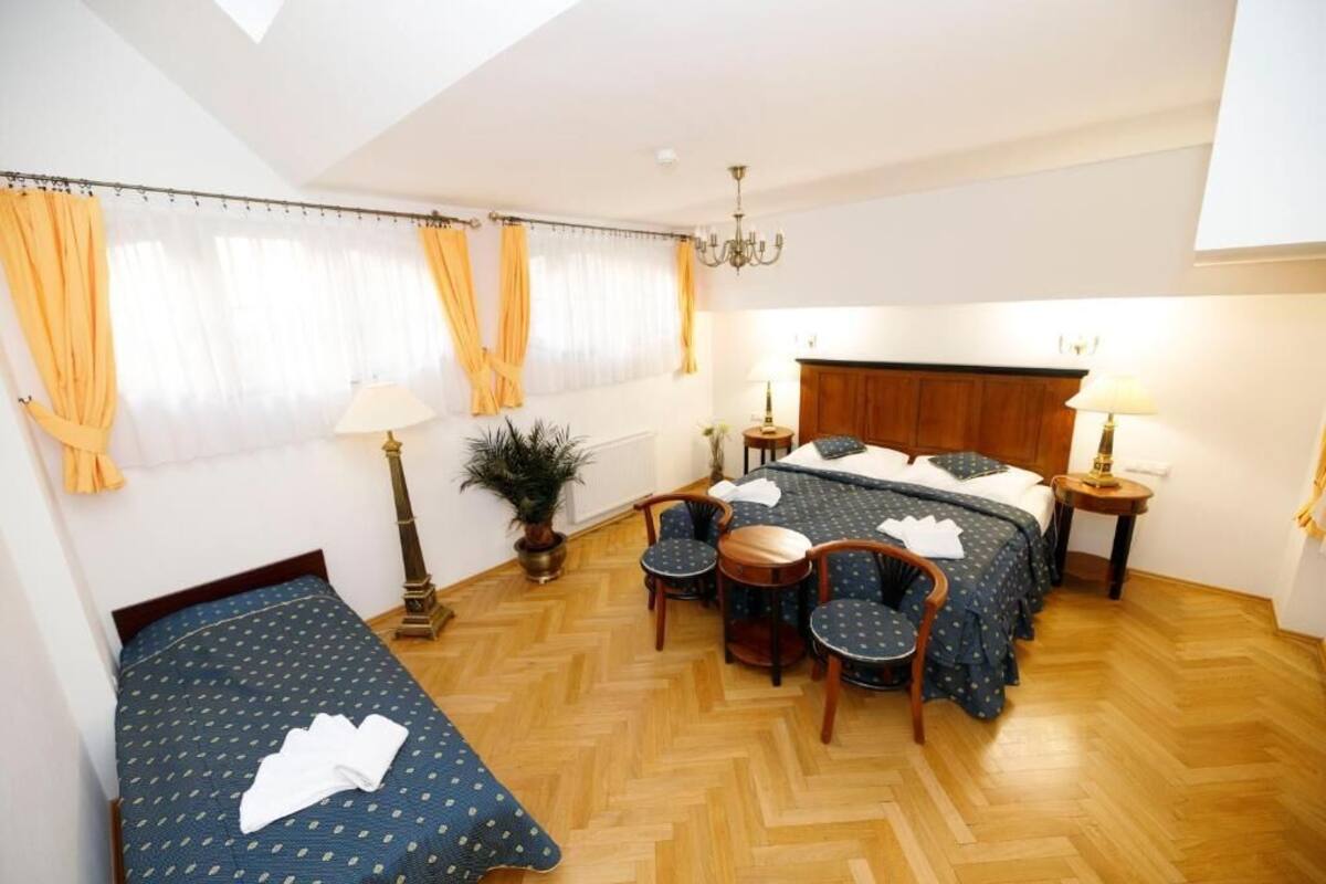 A room with a bed, two chairs, a table, a plant, and a chandelier.