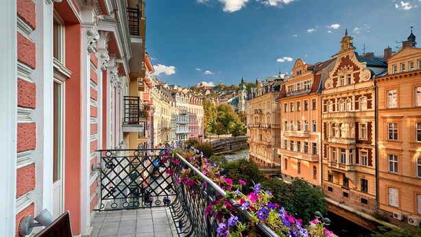 Un balcón con baranda de metal y macetas de flores, con vista a un río y edificios históricos.