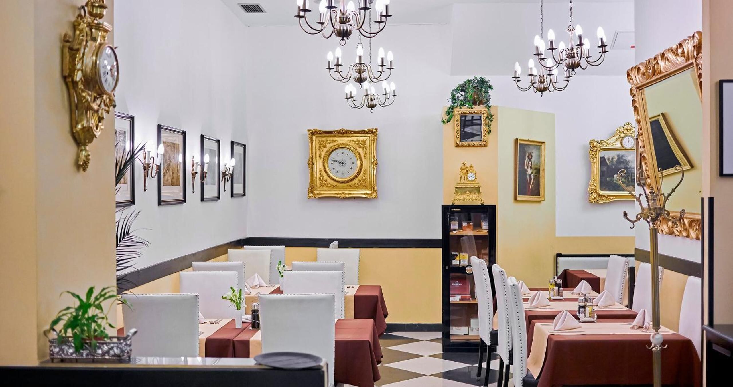 A dining area with tables set for service, framed artwork on the walls, and a chandelier.