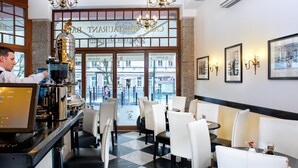 Un restaurante con piso a cuadros, sillas blancas y negras, una zona de bar con una máquina de café y cuadros en la pared.