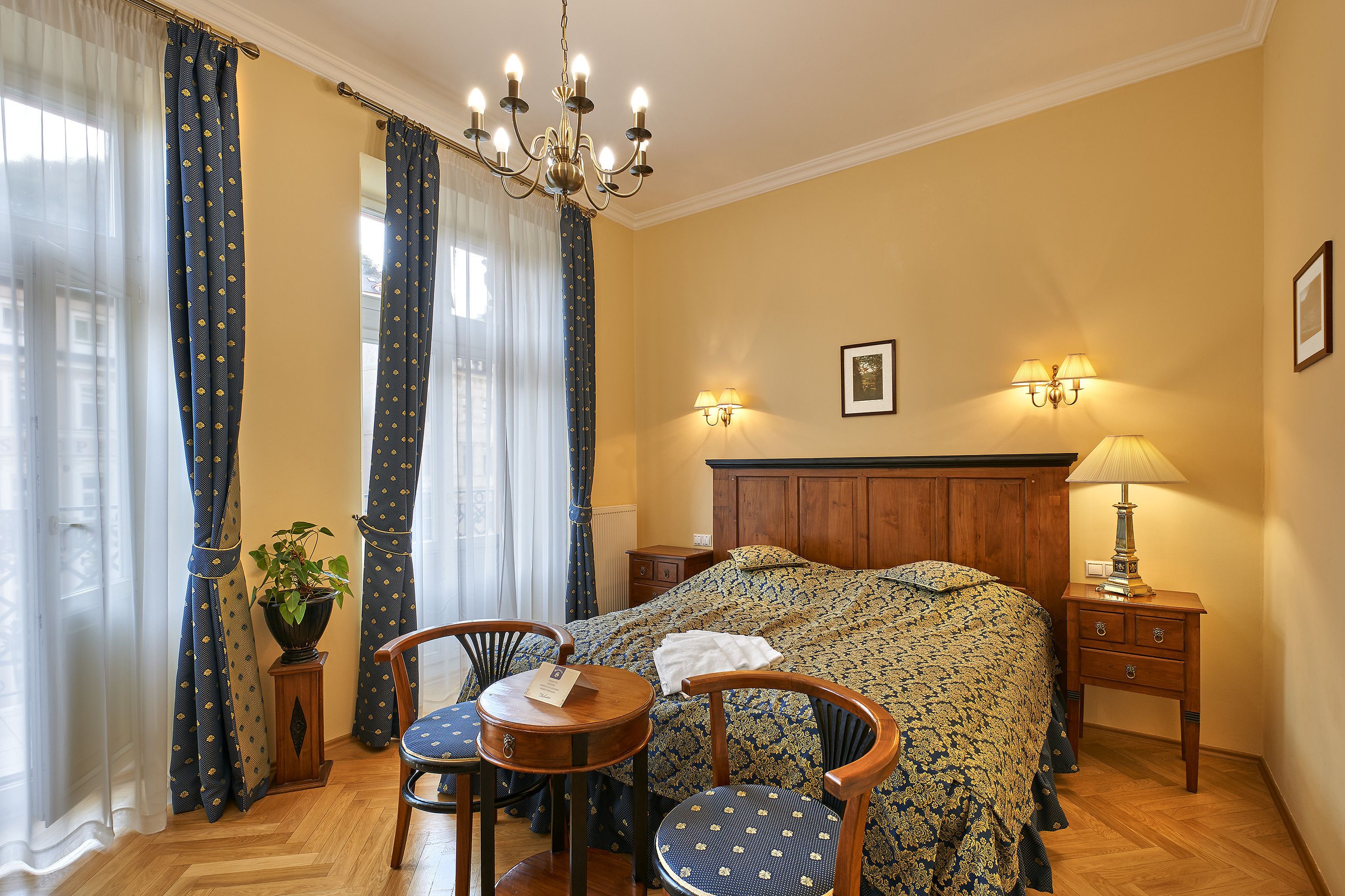 Een slaapkamer met een bed, nachtkastje, lamp, stoel en gordijnen.
