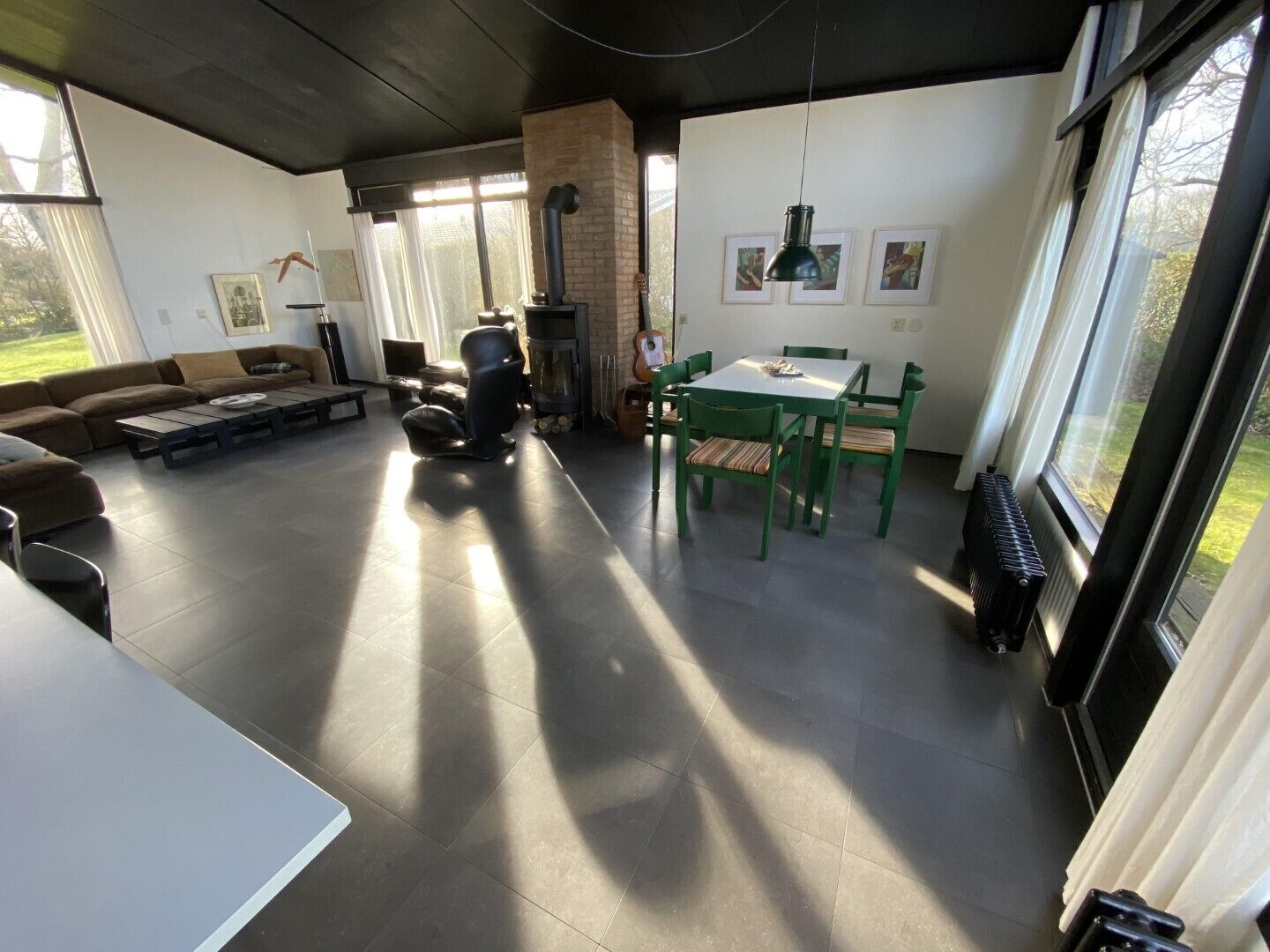 A spacious living area with a sofa, a dining table with chairs, a fireplace, and large windows providing natural light.