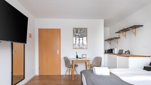 Una habitación de hotel moderna con una cama, un escritorio, una silla, un televisor y una zona de cocina con estanterías.