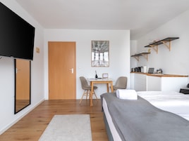 Una habitación de hotel moderna con una cama, un escritorio, una silla, un televisor y una zona de cocina con estanterías.