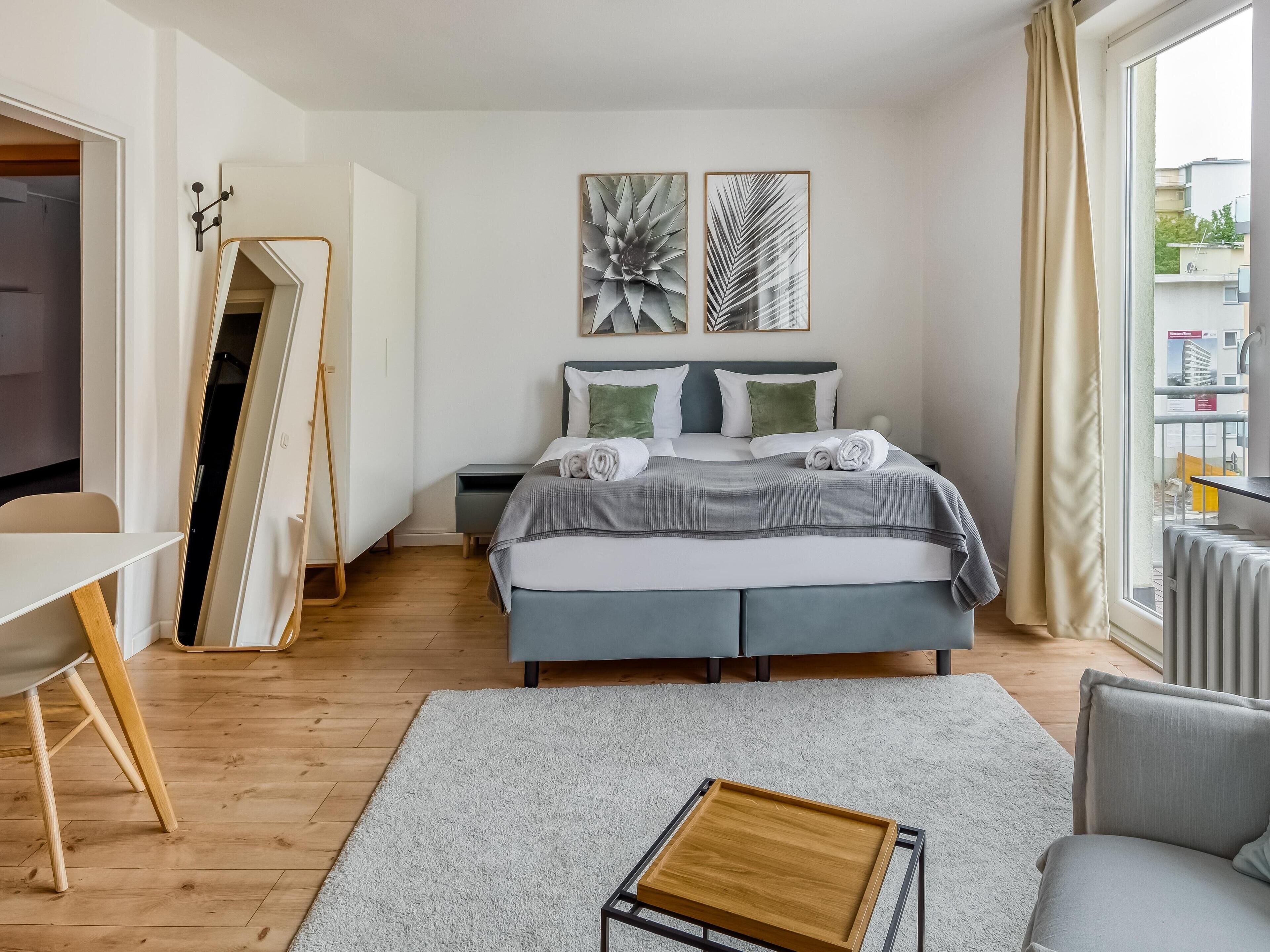 Ein modernes Schlafzimmer mit Bett, Nachttischen, einem Schreibtisch und einem großen Fenster.