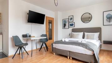 Une chambre d’hôtel moderne, équipée d’un lit, d’un bureau, de deux chaises, d’une télévision et ornée d’œuvres d’art sur les murs.