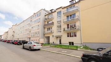 Un filare di edifici residenziali a più piani con balconi, auto parcheggiate e cielo sereno.