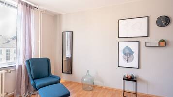Una habitación moderna con una silla azul, un ventanal con cortinas, un mapa del mundo, un reloj y una pequeña planta en un estante.