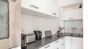Una cocina moderna con gabinetes blancos, encimera negra y electrodomésticos de acero inoxidable, incluyendo una cafetera y un tostador.