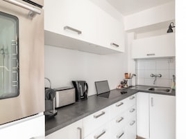 Una cocina moderna con gabinetes blancos, encimera negra y electrodomésticos de acero inoxidable, incluyendo una cafetera y un tostador.