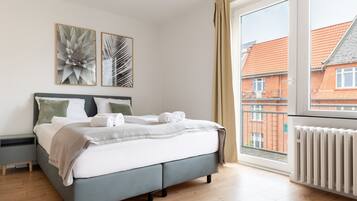 Una camera da letto moderna con un letto grigio, lenzuola bianche e due opere d'arte astratte appese alle pareti.