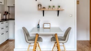 Una cocina moderna con armarios blancos, encimera de madera y un comedor con mesa blanca y dos sillas grises.