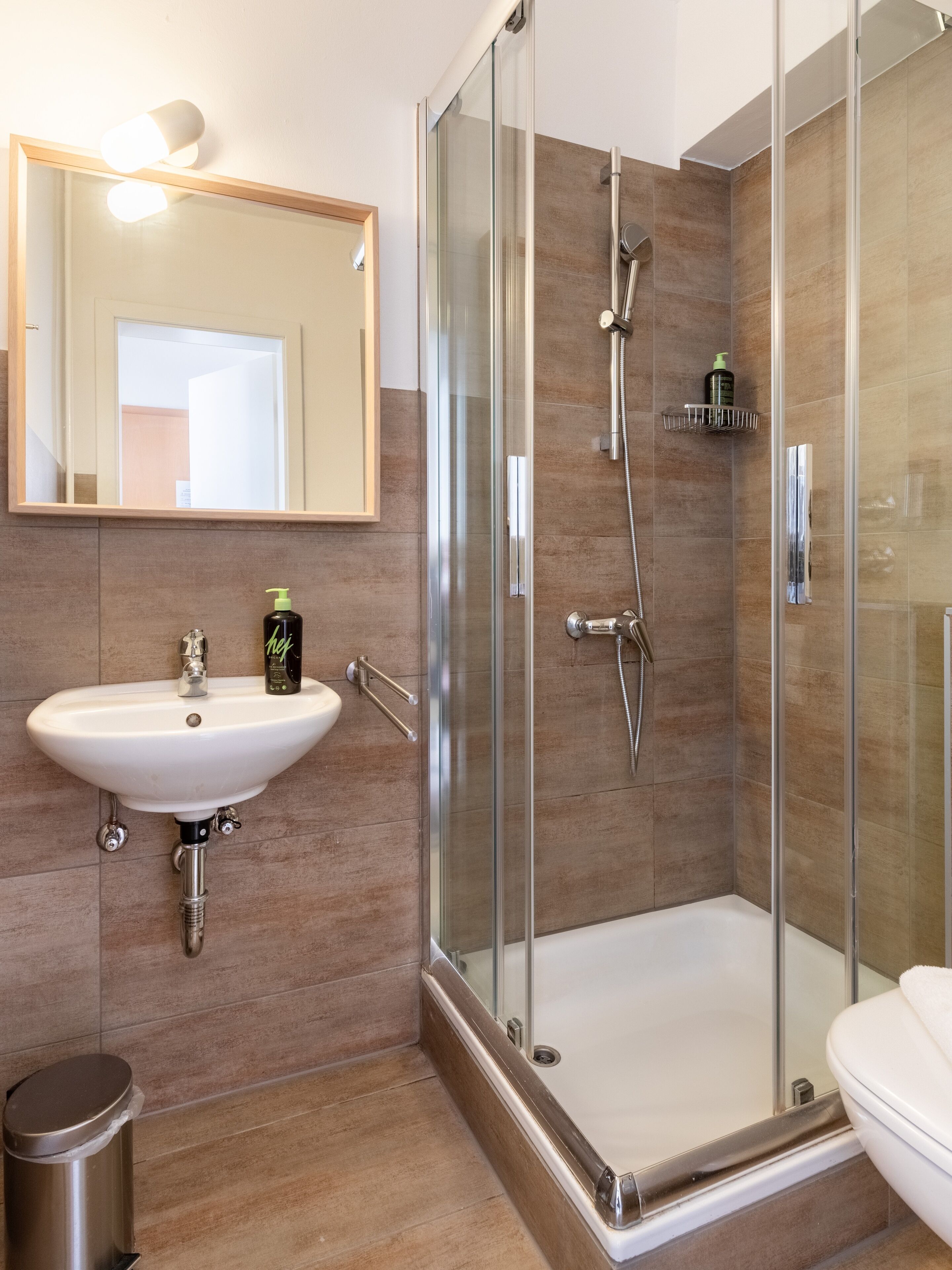 Ein modernes Badezimmer mit einer gläsernen Duschkabine, einem weißen Waschbecken und einem Spiegel darüber.