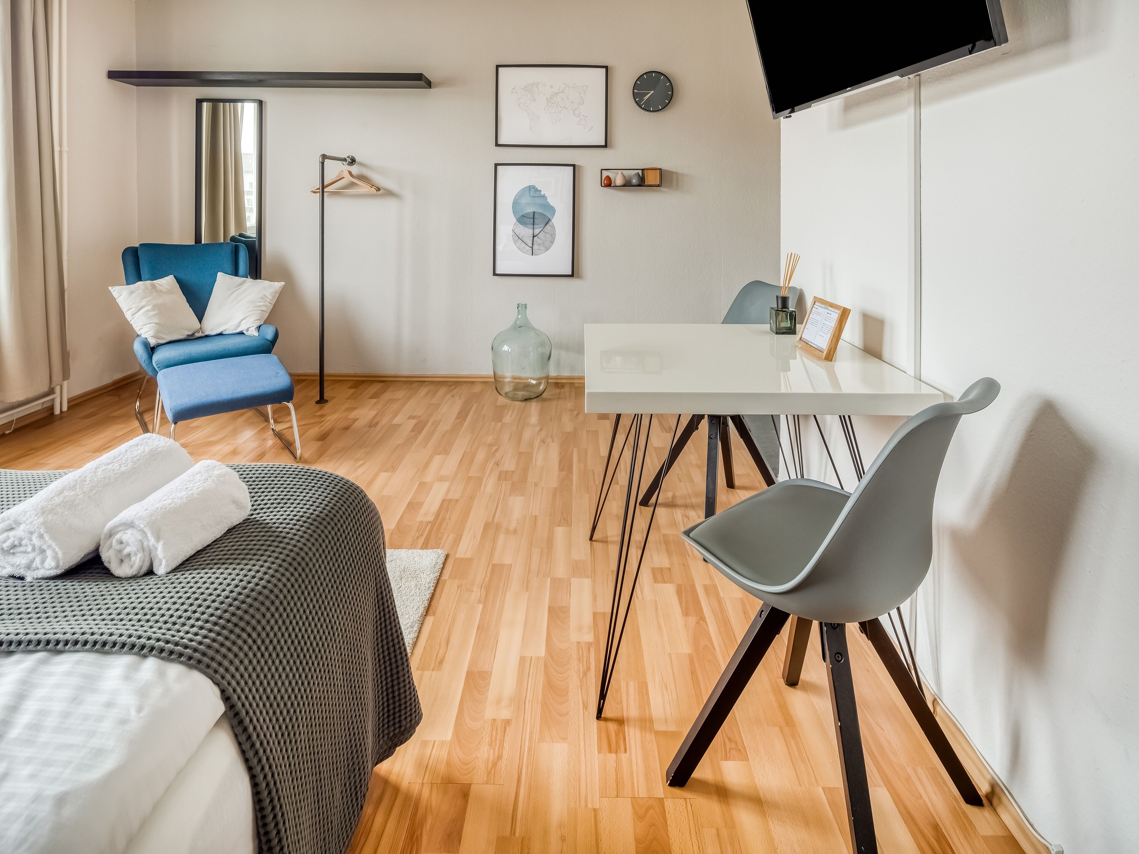 Una camera d'albergo moderna con un letto, una scrivania, una sedia, una TV e un'ampia finestra.