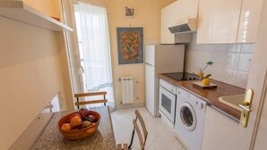 A compact kitchen with a dining table, a bowl of fruit, a washing machine, and a radiator.