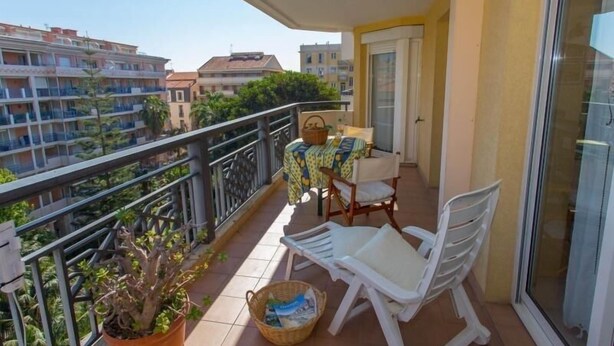 A balcony with a table and chairs, a potted plant, and a view of surrounding buildings.