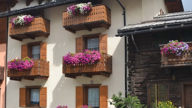 A building with multiple balconies adorned with flower boxes, a stone wall with a sign, and a parking area.