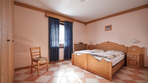 A bedroom with a wooden bed, a chair, a nightstand, and a window with curtains.