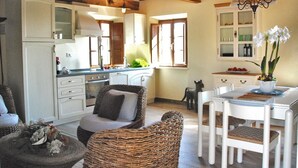 A cozy kitchen with white cabinets, a dining area with wicker chairs, and a chandelier. - Casale Olea (Massarosa)