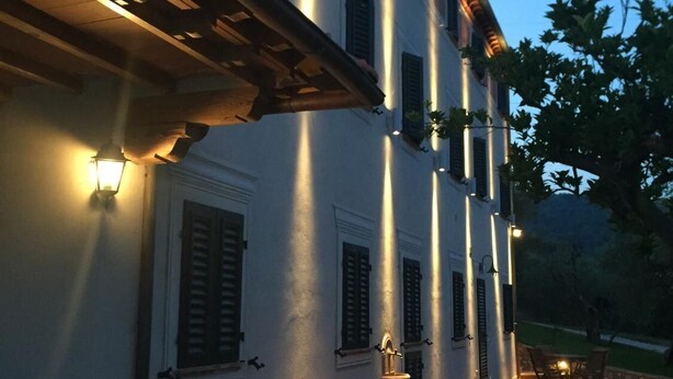 A building with multiple windows and doors, a covered outdoor area with a table and chairs, and a well-lit exterior. - Casale Olea (Massarosa)