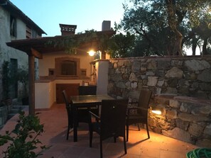 An outdoor patio area with a stone wall, a table with chairs, and a built-in barbecue grill. - Casale Olea (Massarosa)