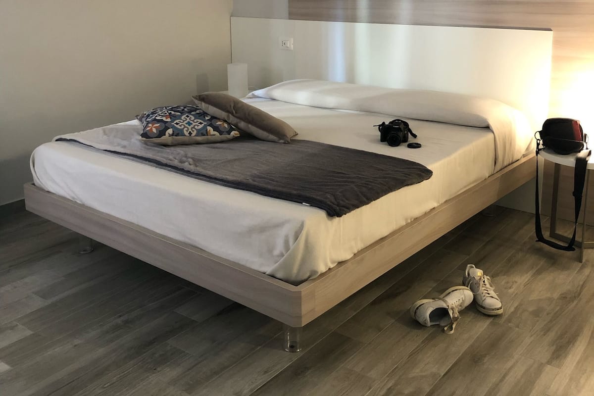 Un dormitorio moderno con cama, almohadas, una mesita de noche y una bolsa.