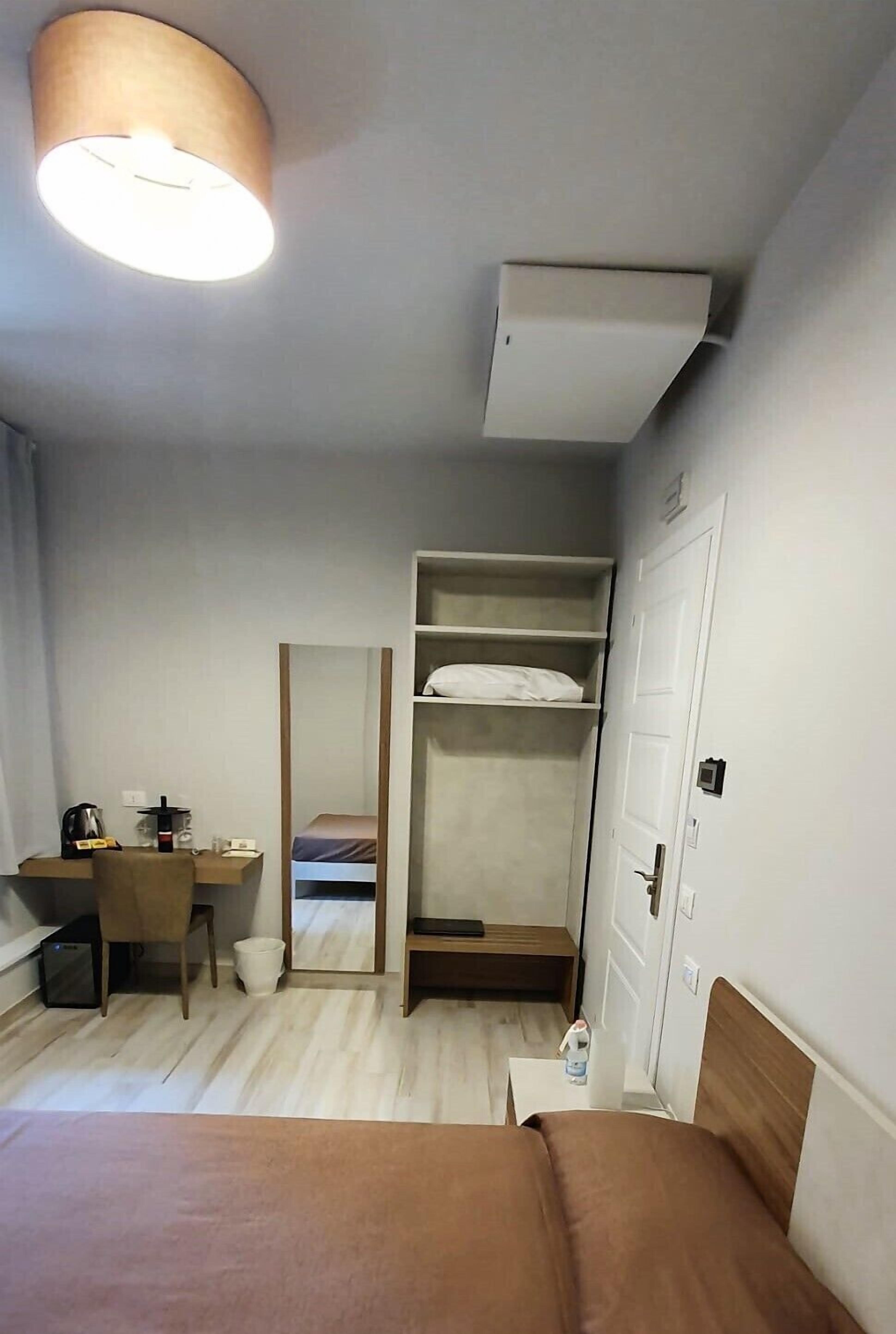 A hotel room with a bed, a desk, a chair, a wardrobe, and a mirror.